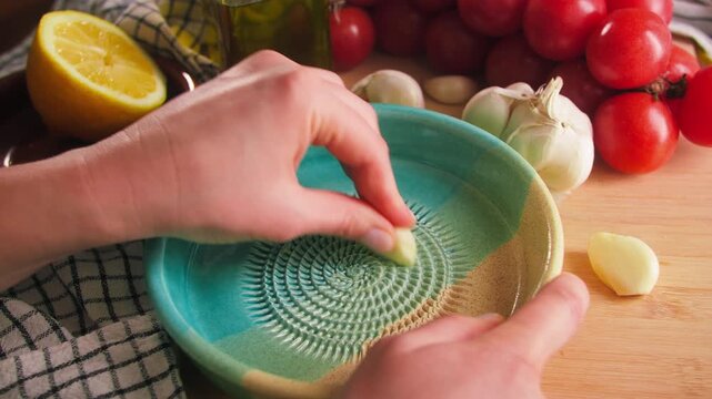 Hand grating fresh garlic on ceramic garlic grater plate, traditional Spanish plato rallador. High quality 4k footage