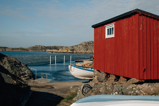 Red wooden house with boathouse and sheds on rocky shoreline
