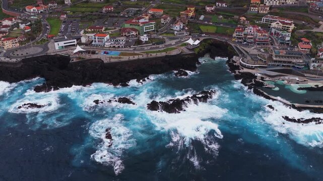 Aerial view of Madeira coastal town with turquoise waves and rocky cli