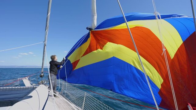 Slow motion close up of colorful spinnaker sail being hoisted on sailing yacht in Croatia, capturing dynamic fabric movement, vibrant colors and detailed nautical action in bright summer conditions
