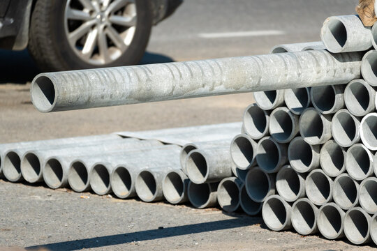Large stack of galvanized metal pipes piled at outdoor construction site.