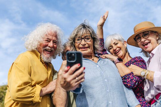 Group of joyful elderly people smiling and posing for a selfie using a mobile phone, enjoying community and modern technology