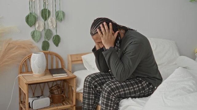 Man sitting on bed covering face with hands, rubbing temples, visible bare hands and wristwatch in building bedroom; fatigue stress reflection.