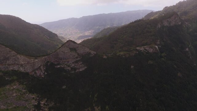 Aerial view of forested mountain valley in Madeira with distant settle