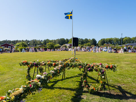 Traditional Swedish Midsummer celebration scene with decorated maypole in the foreground. Cultural summer festival in Sweden, symbolizing heritage, community, and seasonal traditions.