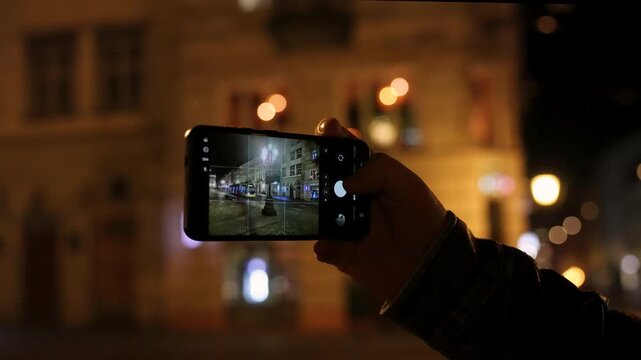 Person filming night city street with tram on smartphone