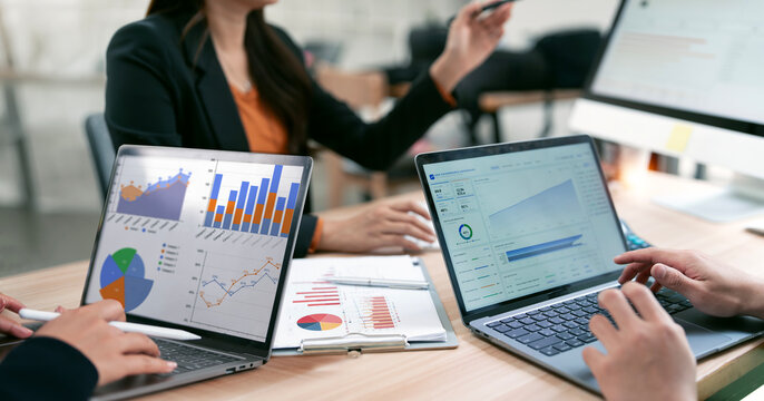 Professional team collaborating on data analysis with laptops and financial charts in a modern office setting.