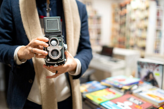 Person holding vintage twin-lens reflex camera browsing books in a second-hand bookstore