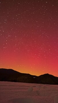 Vertical time lapse of red aurora borealis and stars over winter mountain landscape