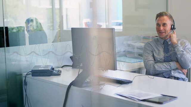 Man adjusting headset and initiating business call, glass partition reflecting seated colleague