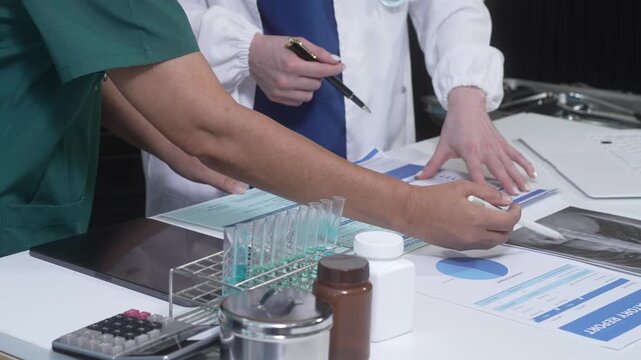 Medical staff in scrubs and lab coat reviewing paperwork and charts at a clinic desk with test tubes, pill bottles and medical reports, teamwork and diagnosis concept