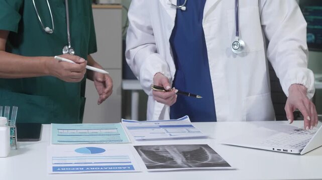 Doctors reviewing medical reports and chest x-ray on desk, using laptop and lab items in clinical setting; teamwork and diagnosis concept.