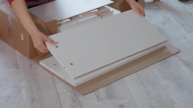 Caucasian Woman Inspecting Furniture Panels On Floor, Checking Holes And Edges, Counting Hardware And Tools Beside Her, Careful Preparation Before Assembly, Bright Renovation Space