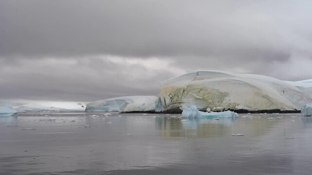 Cinematic moves slowly left past a massive ice cliff stained with orange and green penguin guano at Georges Point, Rong&eacute; Island, Antarctica