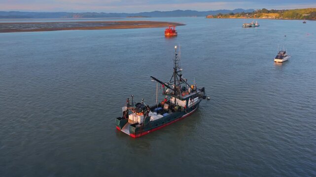 A fishing trawler with crates of catch on the water near a sandbar and distant hills in Kawhia Harbour, Kawhia, Waikato, New Zealand The vessel is preparing to moored.