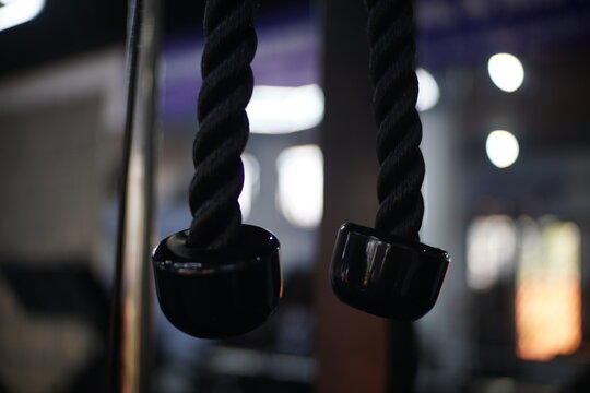 Close-up of black twisted rope handles with rubber caps, gym equipment used for strength training exercises.