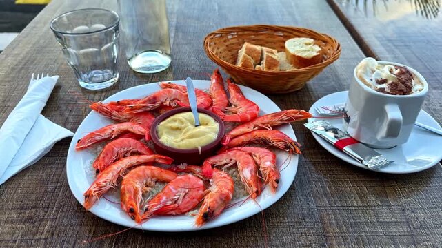 Smooth cinematic gimbal push-in toward plate of fresh cooked prawns with aioli sauce bread basket and coffee at outdoor terrace restaurant in Le Croisic France