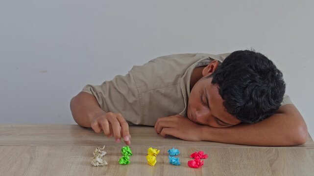 Young man with ocd meticulously arranging crumpled paper balls in row while resting head on desk