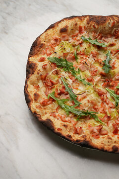 Top View of Gourmet Neapolitan Pizza with Ham and Arugula on Marble Background. Freshly baked artisan pizza with crispy charred crust, diced ham, melted cheese, and fresh arugula
