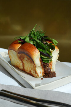 Gourmet Pulled Beef Slider with Fresh Herbs on Toasted Brioche Bun. Close-up of a delicious slow cooked shredded beef sandwich in a golden brioche roll, garnished with cilantro and dill