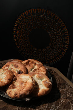 Freshly Baked Oriental Flatbreads on Marble Table. Group of traditional golden-brown flatbreads, pita or naan served on a marble table with a dark, ornate background