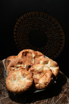 Freshly Baked Oriental Flatbreads on Marble Table. Group of traditional golden-brown flatbreads, pita or naan served on a marble table with a dark, ornate background