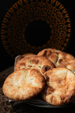 Freshly Baked Oriental Flatbreads on Marble Table. Group of traditional golden-brown flatbreads, pita or naan served on a marble table with a dark, ornate background