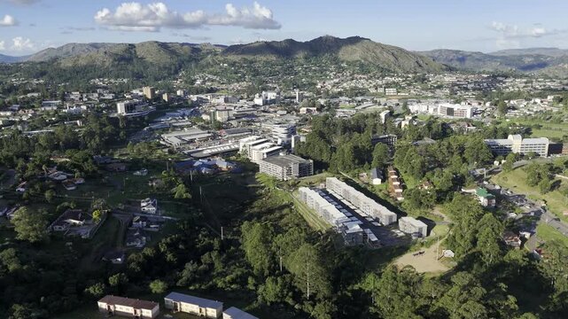 Drone orbits left over green hill with view of city in the distance in the late afternoon before sunset in mountain town of Mbabane, Eswatini