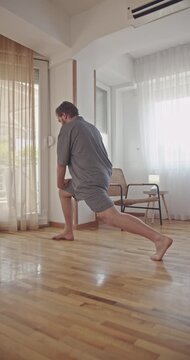 A man performs a series of lunges and toe touches to warm up his body at home. He focuses on his flexibility and fitness as part of his daily routine.