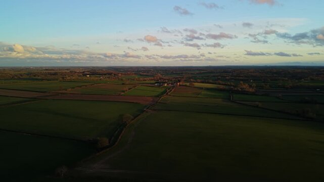 Aerial of golden hour light passing over farmers fields of Harrogate in North Yorkshire with soft colours and orange glow and shadows
