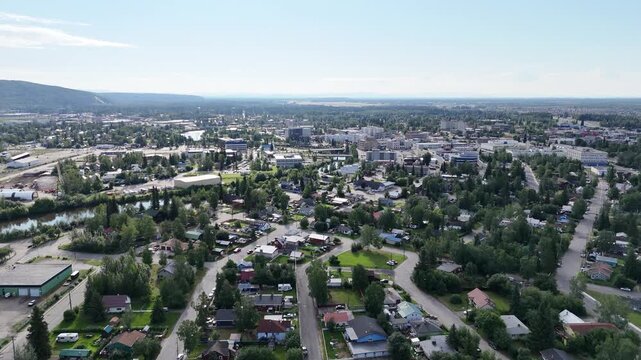 Scenic aerial view flying sideways over fairbanks, alaska, showcasing the sprawling city with its downtown buildings, residential neighborhoods, and the winding chena river on a bright, sunny day