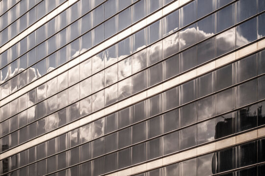 Modern office architecture with glass facade building windows showing reflection stripes and clouds for corporate business abstract backdrop