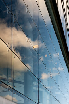 Modern office building windows with reflection on glass facade under clouds and sky showing architecture texture for corporate business backdrop