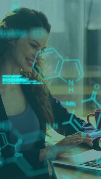 Vertical video: Woman typing laptop starting holo code+mol overlay moving for R and D sipping red mu