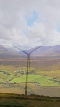 Vertical video: Wind turbine rotating slowly on hillside, wind powering renewable energy for farms