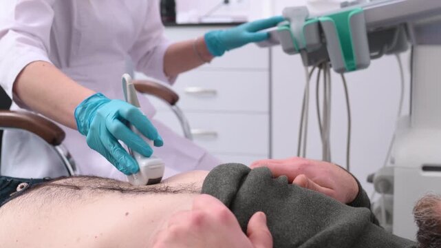 A doctor performs an ultrasound of the abdominal cavity of a male patient lying on a couch.