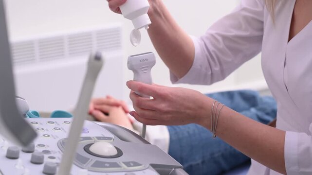 An endocrinologist examines a patient's thyroid gland using an ultrasound machine. The doctor applies gel to the ultrasound sensor.