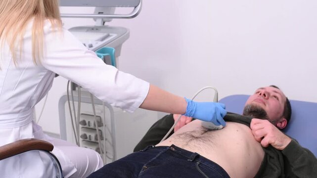 A doctor performs an ultrasound of the abdominal cavity of a male patient lying on a couch.