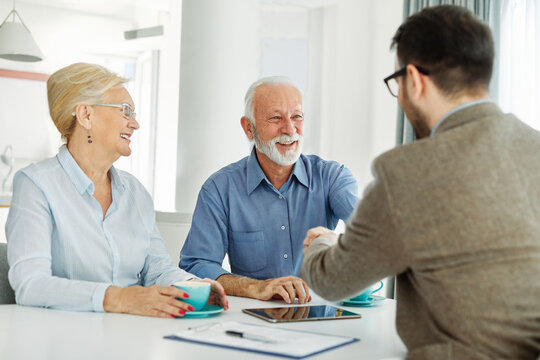 Portrait of a businessman or real estate agent or doctor shaking hands and signing a deal contract with senior couple in his office