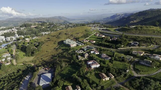 Drone facing south, orbits left as highway cuts through hills in the late afternoon before sunset in mountain town of Mbabane, Eswatini