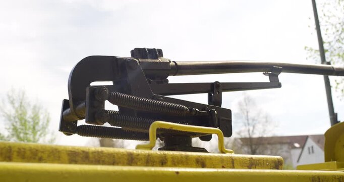 Close up of a mechanical pantograph with tension springs on a yellow vehicle roof against bright sky