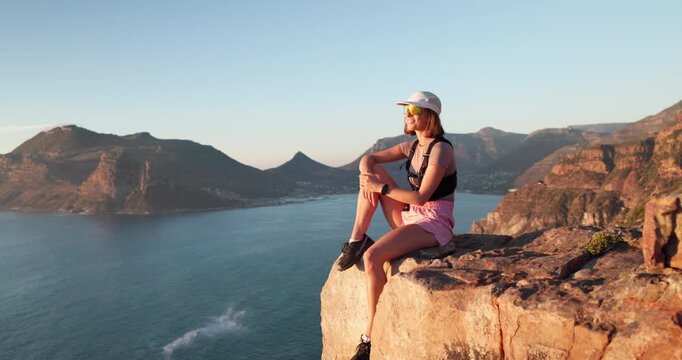 Woman, hiking and thinking with rest on mountain with ocean view, space and relax on summit. Girl, outdoor and break on peak, rocks and perspective for trekking, adventure or sunglasses in summer