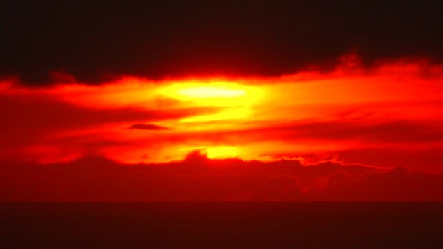Sunset fiery horizon intense red clouds moving over dark sea creating a dramatic atmosphere.
