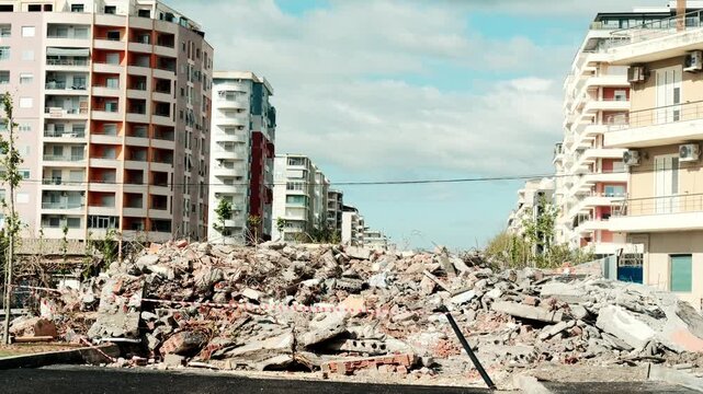 Handheld shot Pile of construction debris and demolished building remains between apartment houses in city. Urban demolition site with rubble, broken concrete, bricks and caution