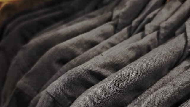 Extreme close up of dark gray linen shirts arranged on hangers. The focus slowly shifts along the row, highlighting the fabric texture