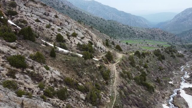 Aerial push in shot of hikers on a narrow mountain trail along a rushing river with snow patches in a misty gorge, Kazakhstan, Sayram-Ugam State National Nature Park.
