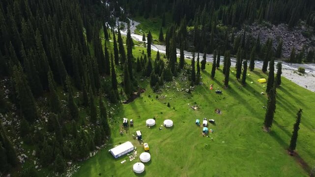Top down aerial tracking shot over a traditional nomadic yurt camp and colorful tents in a green mountain valley, Kyrgyzstan, Karakol.

