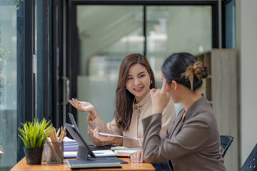 Fototapeta premium Two Asian businesswomen collaborating and discussing financial project on laptop and documents in office.