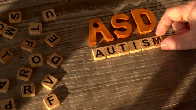 ASD abbreviation and a hand arranging text: Autism Spectrum Disorder. Wooden letters and tiles with letters, rustic wooden background.