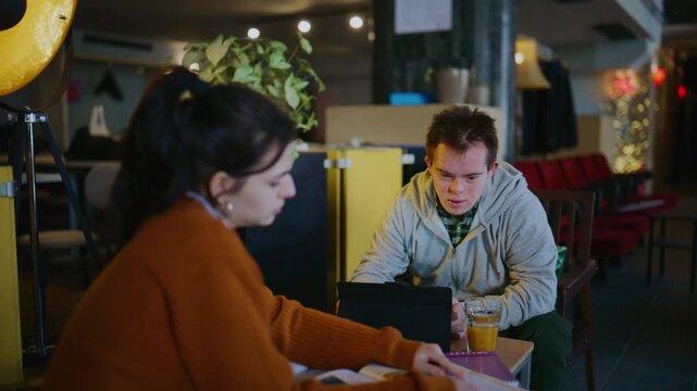 Young students collaborate on a project in a cozy cafe setting. They are engaged in inclusive learning and mutual support.